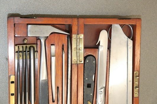 A close-up shot of an open wooden case displaying a selection of metal medicine tools.