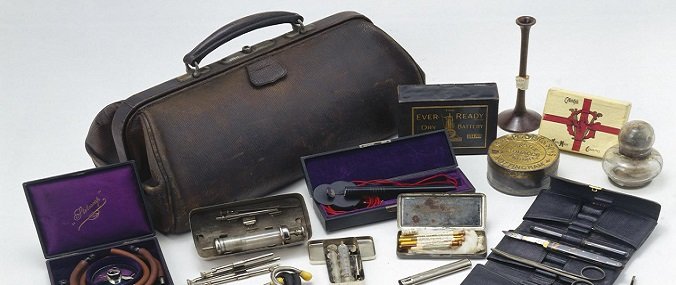 A leather doctor's bag is placed on a white surface, surrounded by medical tools. 