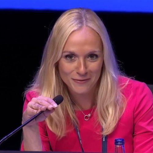 A square photograph of Dr Victoria Tzortziou Brown OBE sitting next to a microphone.