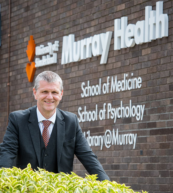 Professor Scott Wilkes in front of a sign for the University of Sunderland's Murray Health School of Medicine.