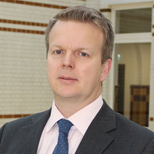 A square head and shoulders photo of Dr Ben Clacy wearing a grey suit.