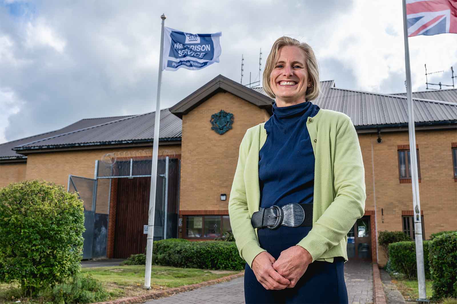 A large photo image of Dr Caroline Watson standing outside a yellow-brick building.