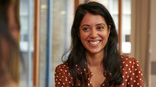 A woman with long dark hair smiles at someone out of shot. 