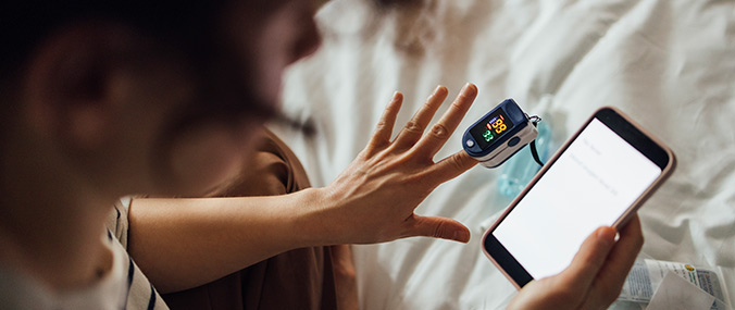 A person is taking their blood pressure using a digital device on their left index finger and checking the reading on their smartphone.