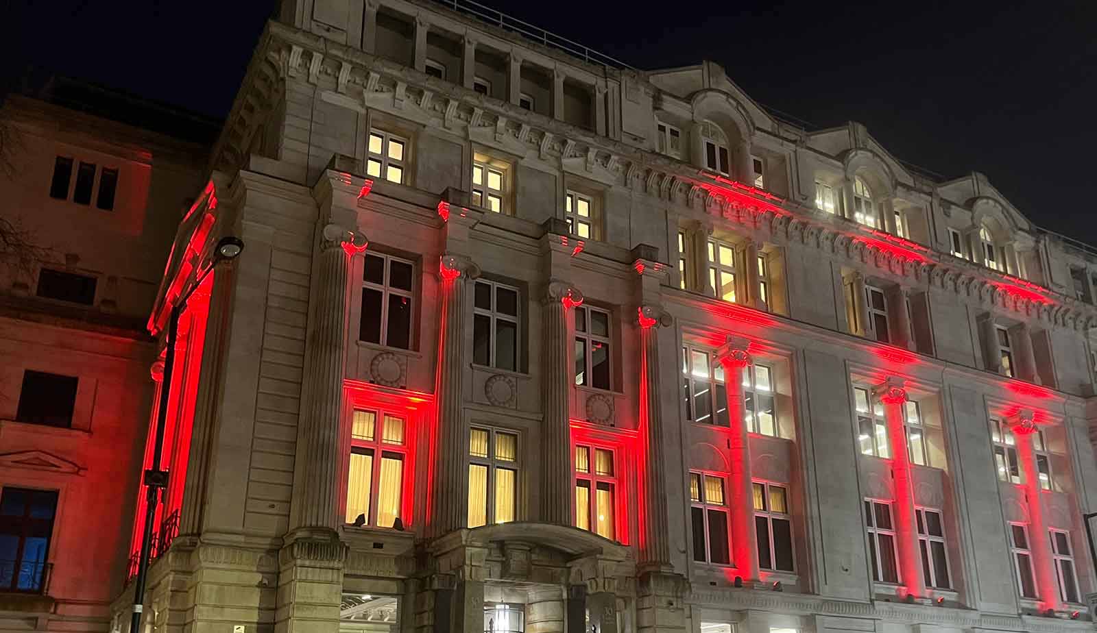 The RCGP 30 Euston Square building lit up with red lights at night.