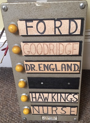 A series of doctors' and nurses' names on labels on a silver metal box, with yellow buttons alongside them.