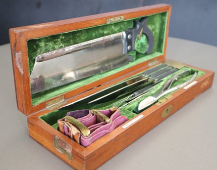 An image of a traditional wooden amputation kit, open to display a set of historic medical tools.