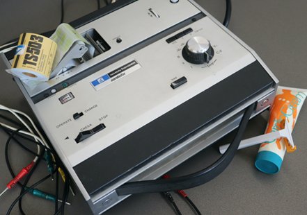 An image looking down on a grey and black ECG machine on a dark grey table.