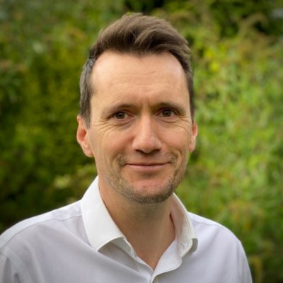 A head and shoulders image of Professor Dom Patterson standing outside with shrubbery behind him.